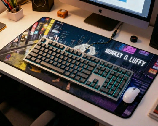 Monkey D. Luffy city desk mat setup with gray RGB mechanical keyboard, white mouse, iMac, speaker, plant, and urban anime artwork.