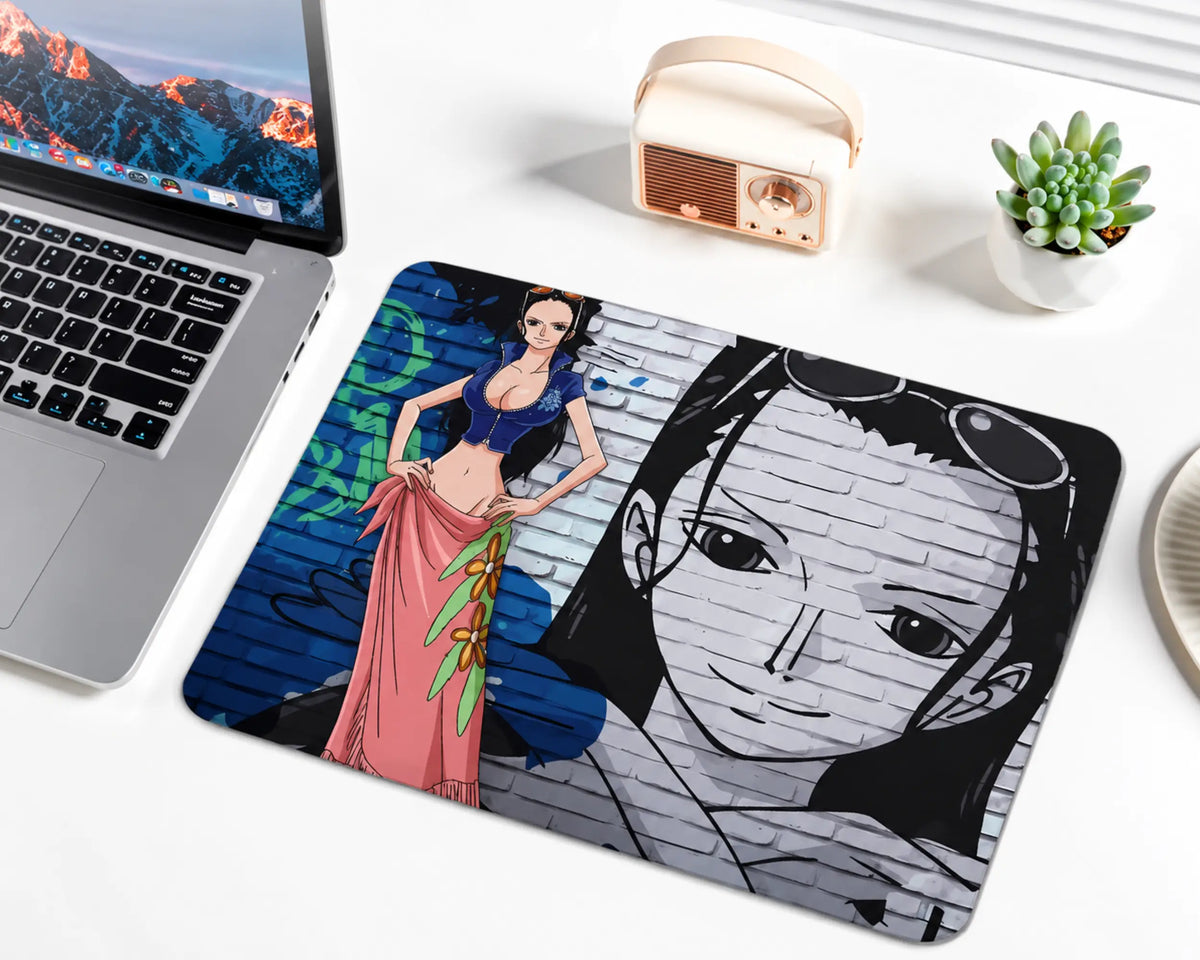Nico Robin from One Piece wearing a blue cropped top and a pink floral skirt, with long black hair and sunglasses on her head, standing against a blue and gray graffiti brick wall with a large monochrome portrait on a gaming mouse pad.