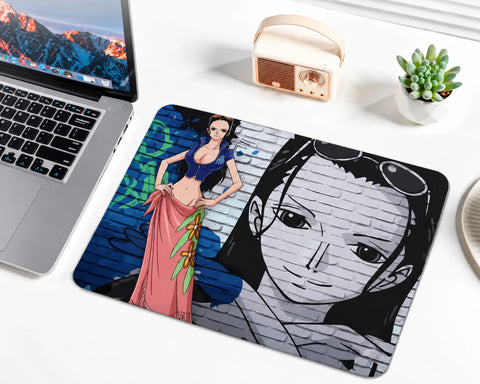 Nico Robin from One Piece wearing a blue cropped top and a pink floral skirt, with long black hair and sunglasses on her head, standing against a blue and gray graffiti brick wall with a large monochrome portrait on a gaming mouse pad.