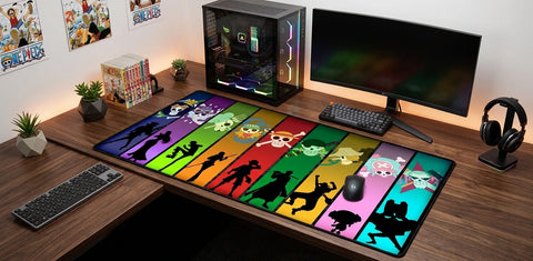 One Piece XXL desk mat with vibrant multicolor panels, displayed on an L-shaped wooden desk with gaming PC, monitor, keyboard, mouse, and anime decor.