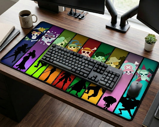 Rainbow colored One Piece crew silhouette desk mat featuring Straw Hat Pirates character panels on a modern gaming desk with full-size mechanical keyboard and mouse