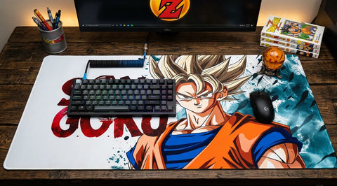 Wooden desk setup with a large Son Goku anime desk mat, mechanical keyboard, and mouse. Includes monitor, pen holder, and small decor items.