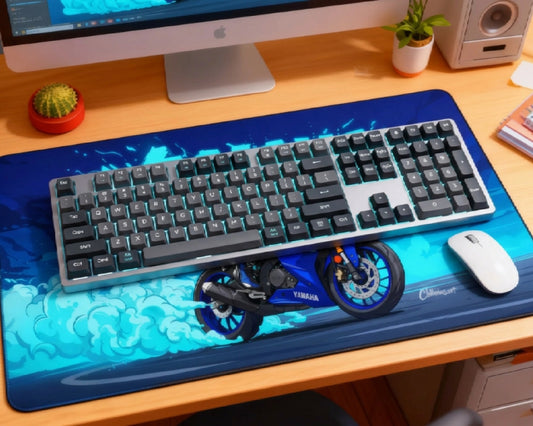 Blue Yamaha motorcycle desk mat setup with gray mechanical keyboard, teal backlighting, white mouse, iMac, cactus, plant, speaker, and wooden desk.